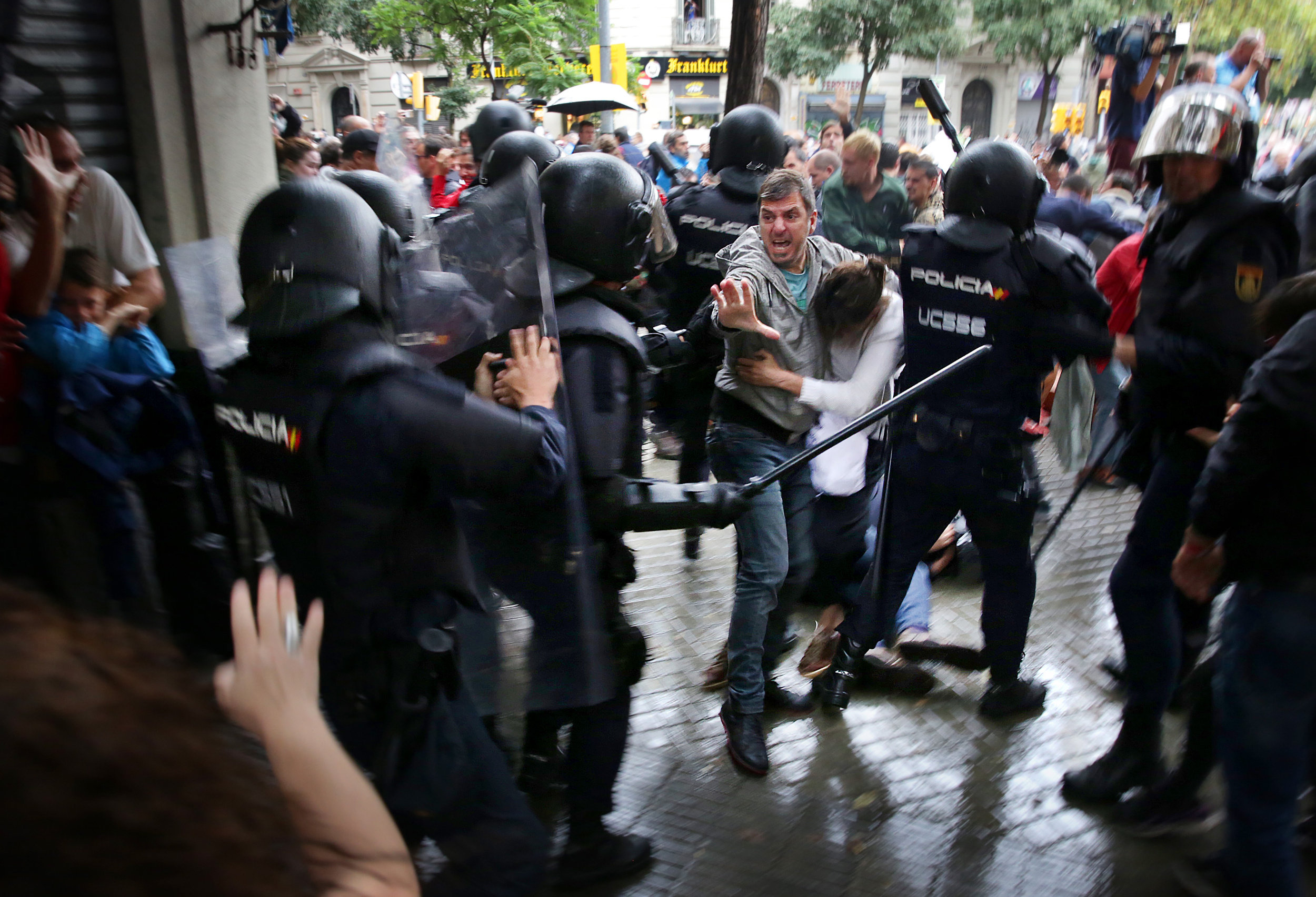 A man shields a woman from the police in Barcelona outside of an independence referendum polling station (by Jordi Play)
